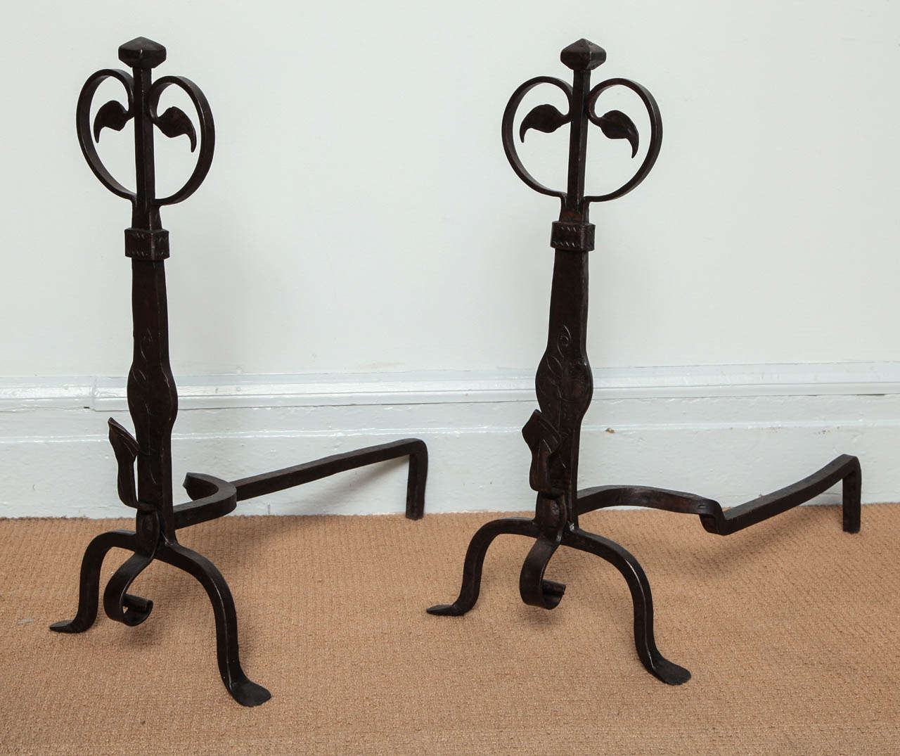 A pair of decorative and good quality wrought iron andirons with paired trailing vine tops on a faceted finial, etched shafts with spit supports, standing on arched feet.  American, circa 1910.