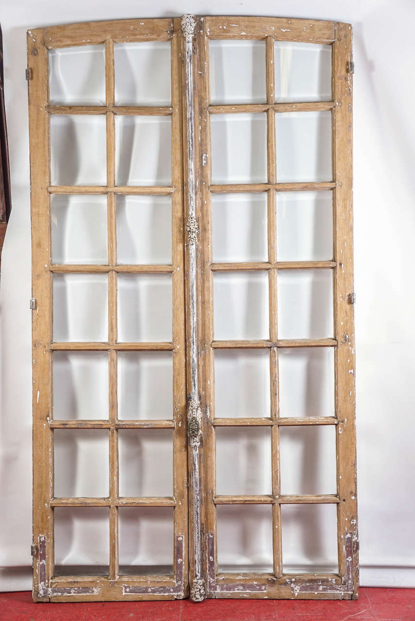 These antique double doors from France with rounded tops have bevelled glass, original cremone bar lock with decorative knob that turns to bolt the bar at top and bottom, and L-shaped inset brackets at the bottoms.  The left door has a rounded male