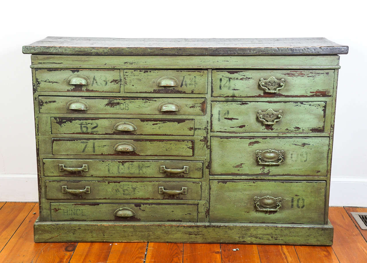 This unique original painted base likely came from a hardware store. Painted on each of the 12 different sized drawers is a letter and number, usually used in a store of this type. The color green is warm a rich and the original top is a nice shade