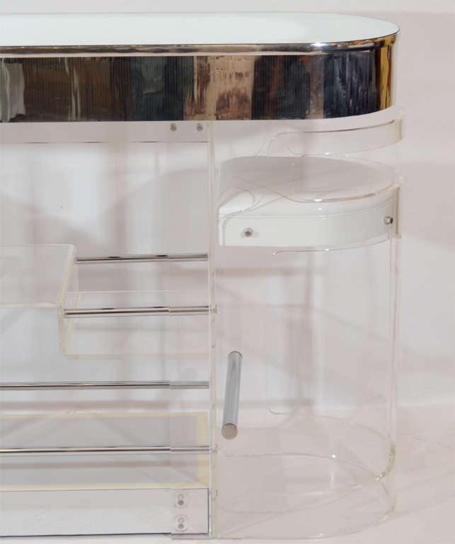 Fabulous lucite bar and stool set. The bar is trimmed and topped in mirror and is illuminated from below. The stools are upholstered in shiny patent white vinyl and fit under the bar in a compact display; note detailed photos. Fun! Located in Las