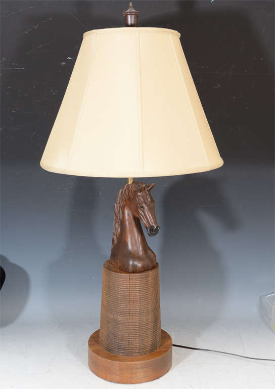 A vintage hand carved wooden lamp with a cylindrical base and an intricately carved horse head at the top.