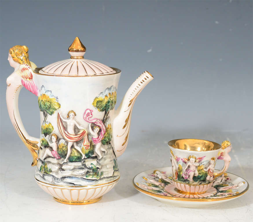 A vintage Capodimonte porcelain tea or espresso set. The set includes six cups and saucers, a tea/espresso pot, covered sugar bowl and milk/cream server. Each is decorated with cherubic figures in idealized landscapes and is marked 