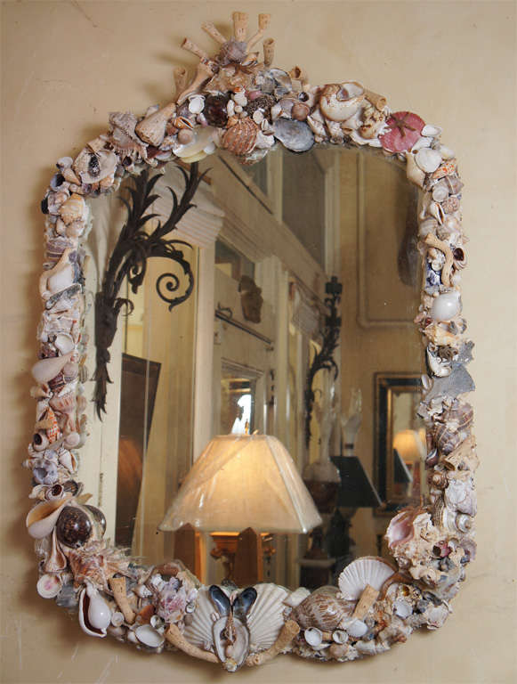 This Mirror from the last half of the 19th century is in a mahogany frame and retains its old mirror plate which is beveled and showing nice old spotting and foxing. The frame has afterwards been decorated with shells, crustatuions, starfish, dried