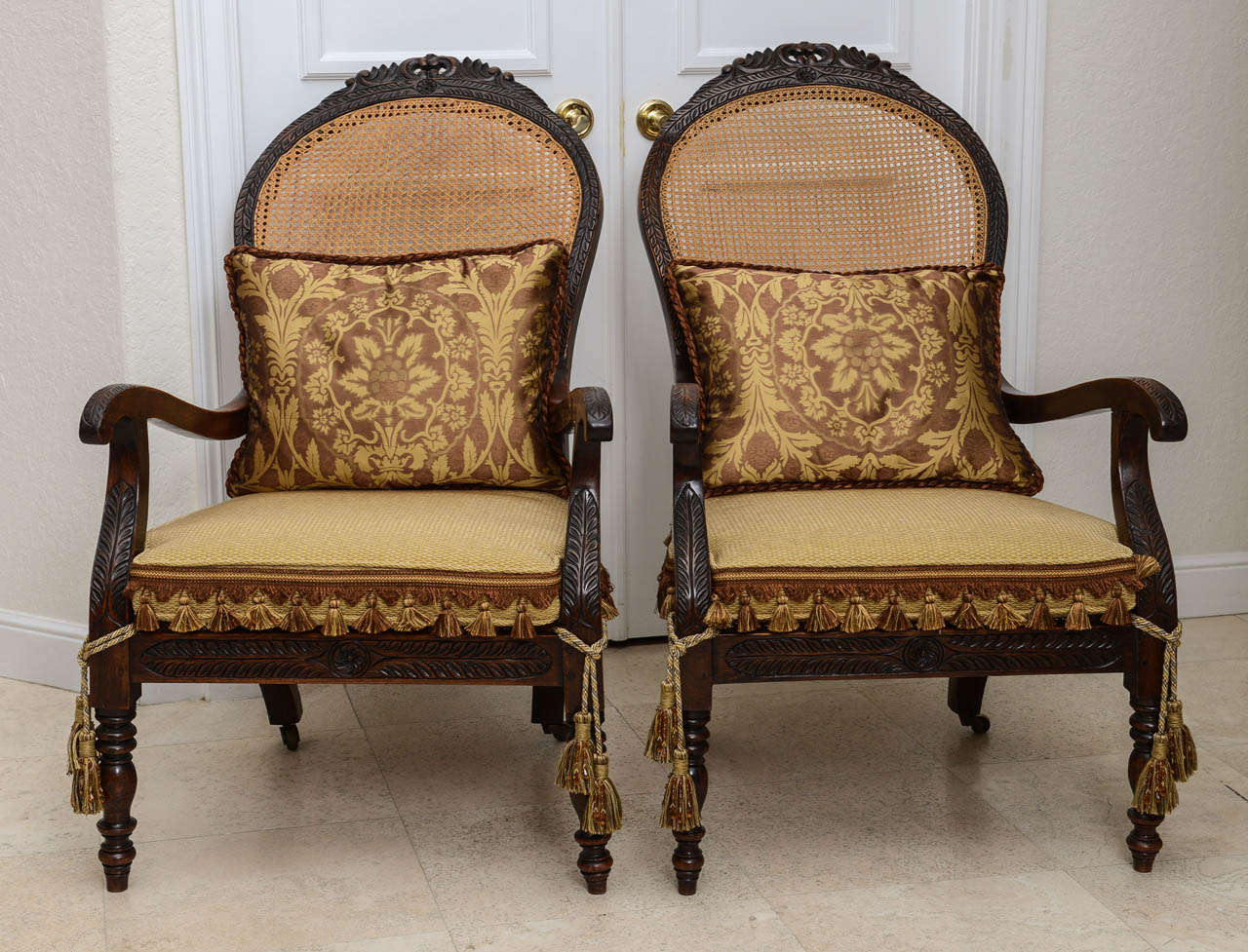 Pair of unusual French armchairs with a pitched back. Beautifully hand carved with cane back and seat with custom seat cushions and tassel ties. Original restored finish.