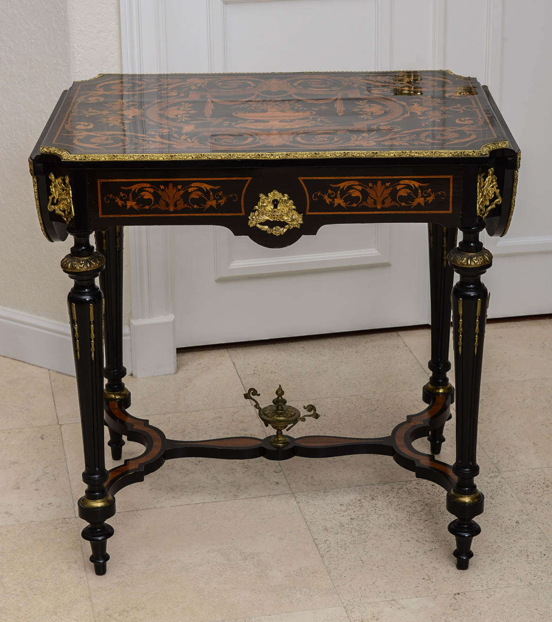 This versatile table has many uses because it is finished on all four side.  Beautiful ebony finish is set off with intricate marquetry & ormolu.  Tapered legs are inset with ormolu, as well as the table surface edge & drop front leaves.  There is a