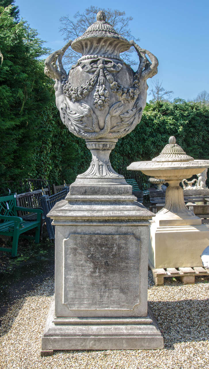 A pair of spectacular, large reclaimed urns with an ornate, neoclassical style. This stone urns feature elaborate decoration including blossoming swags and large ribbons between elegant mermaid figurines reaching to the urn's lids. The bases feature