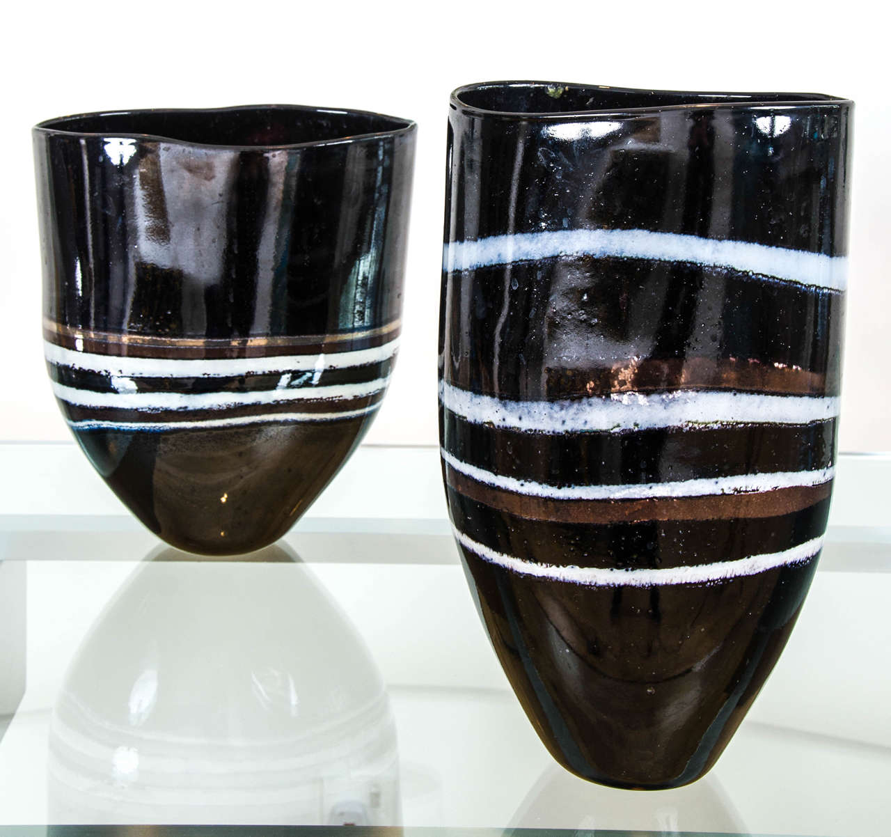 The Netherlands, 1990s
Free-form glass vases with metallic and white bands on an espresso black body,
Each with engraved signature
Larger: H 40 / W 24 / D 16 cm
Smaller: H 33 / W 47 / D 18 cm.