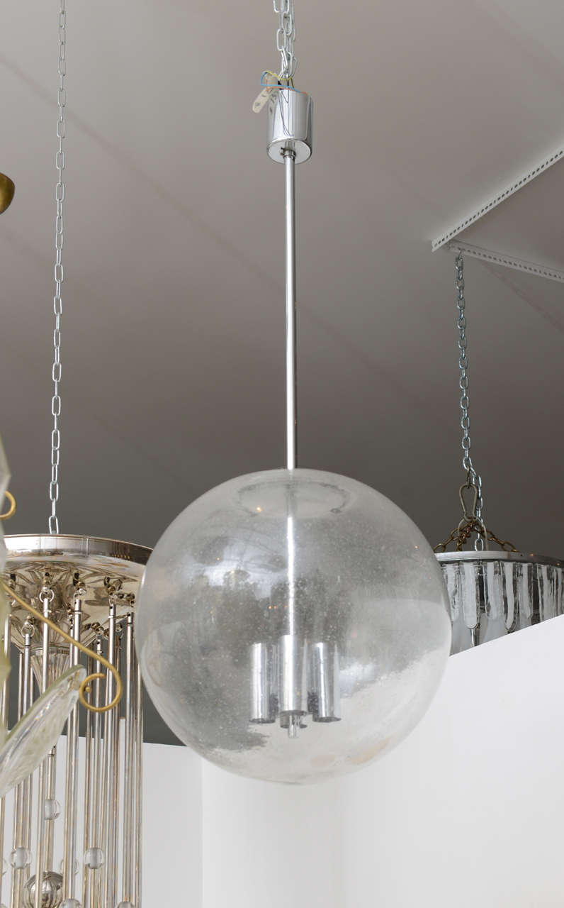 Clear glass globe pendant light fixture with slight bubble pattern throughout.  The fixture has a chrome rod with four tubular chrome sockets. The fixture has been professionally rewired to US standards. We have two available. They are sold