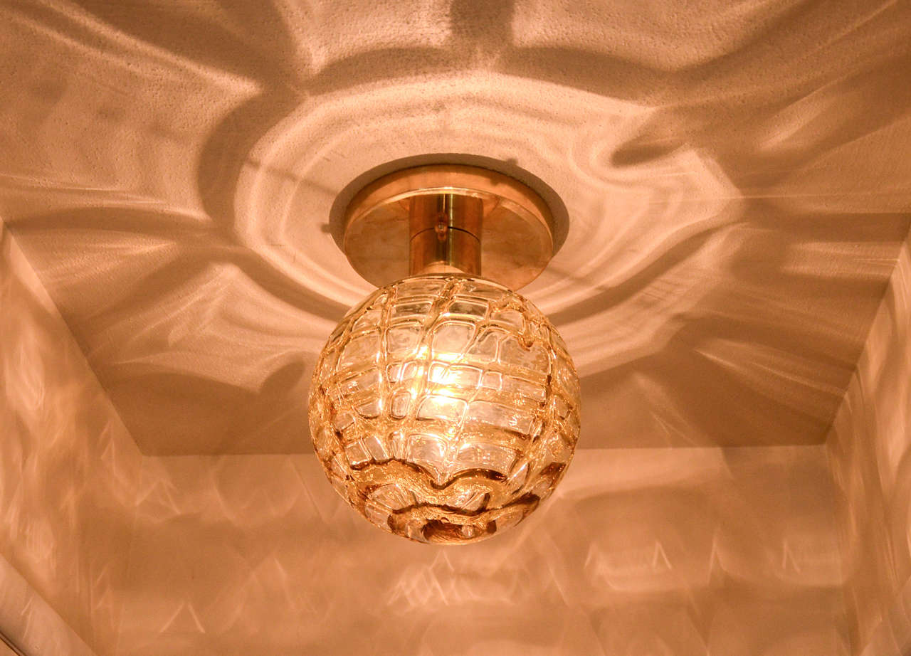 This Large Doria ball flush mount fixture has tones of clear and amber glass. The elegant glass globe is supported by a polished brass base.