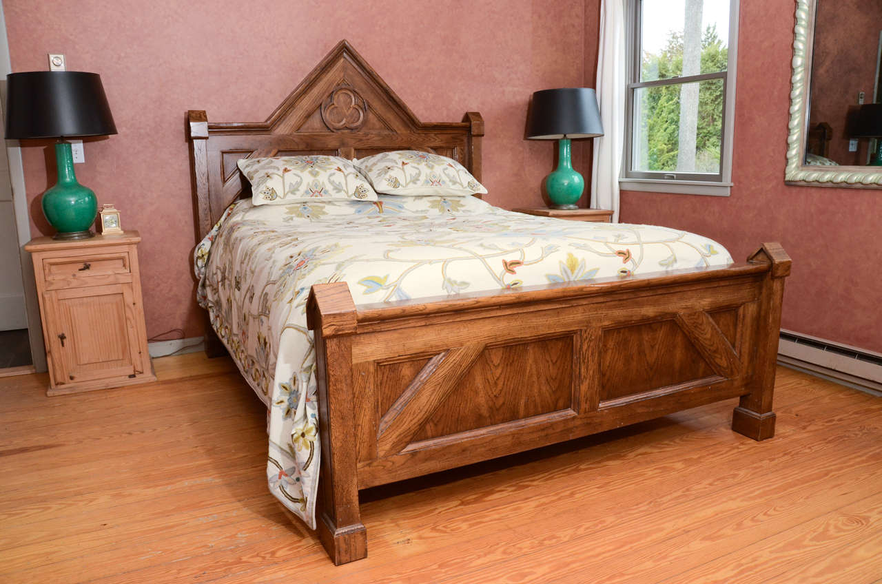 Wonderful queen-size bed in the Gothic style by Baker Furniture Company.  This impressive bed frame has a combination of solid oak hardwood framers with certain flat sections that are veneered.  The headboard features a carved central trefoil. There