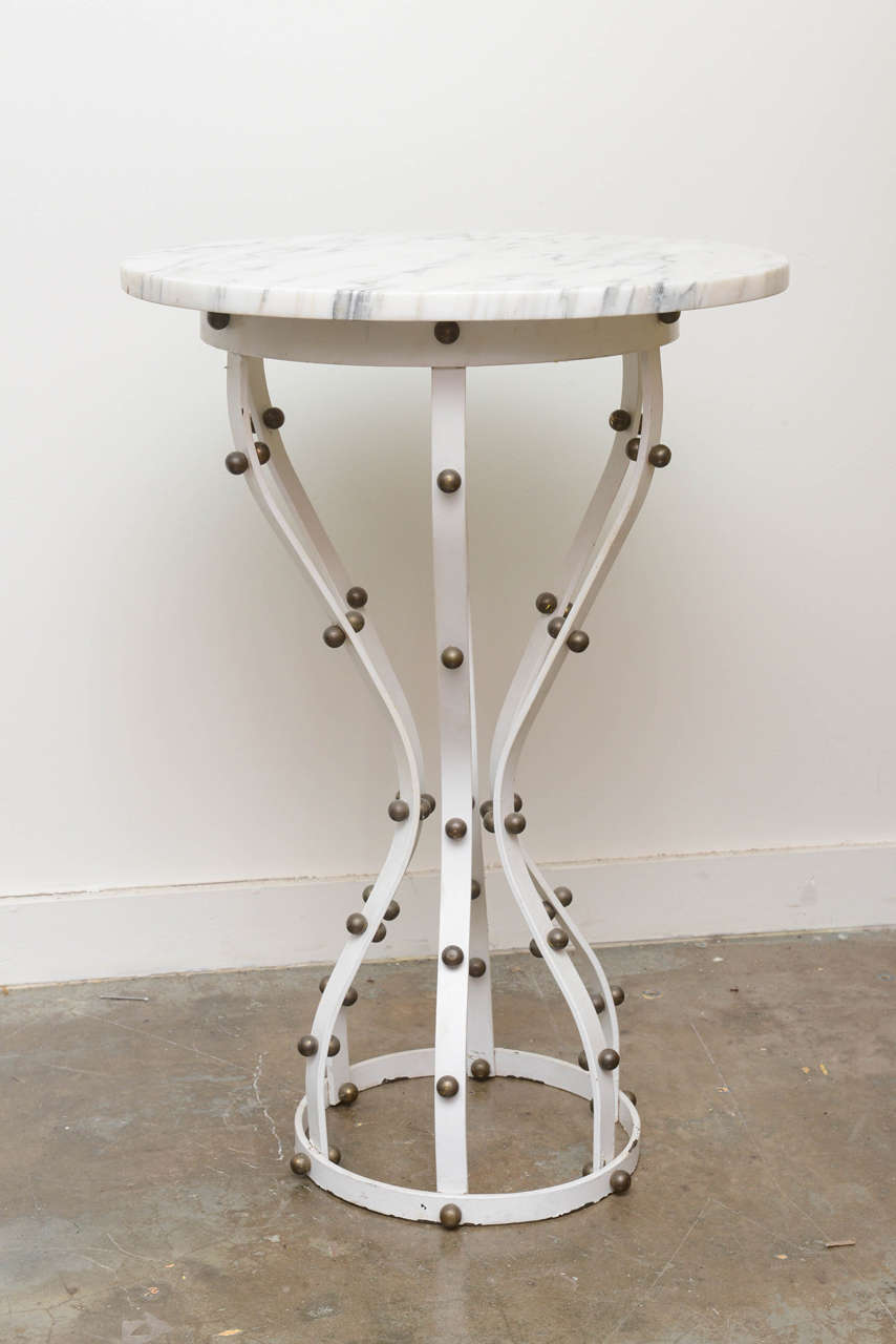 Sleek marble topped, iron hourglass pedestal table with brass ball applications.