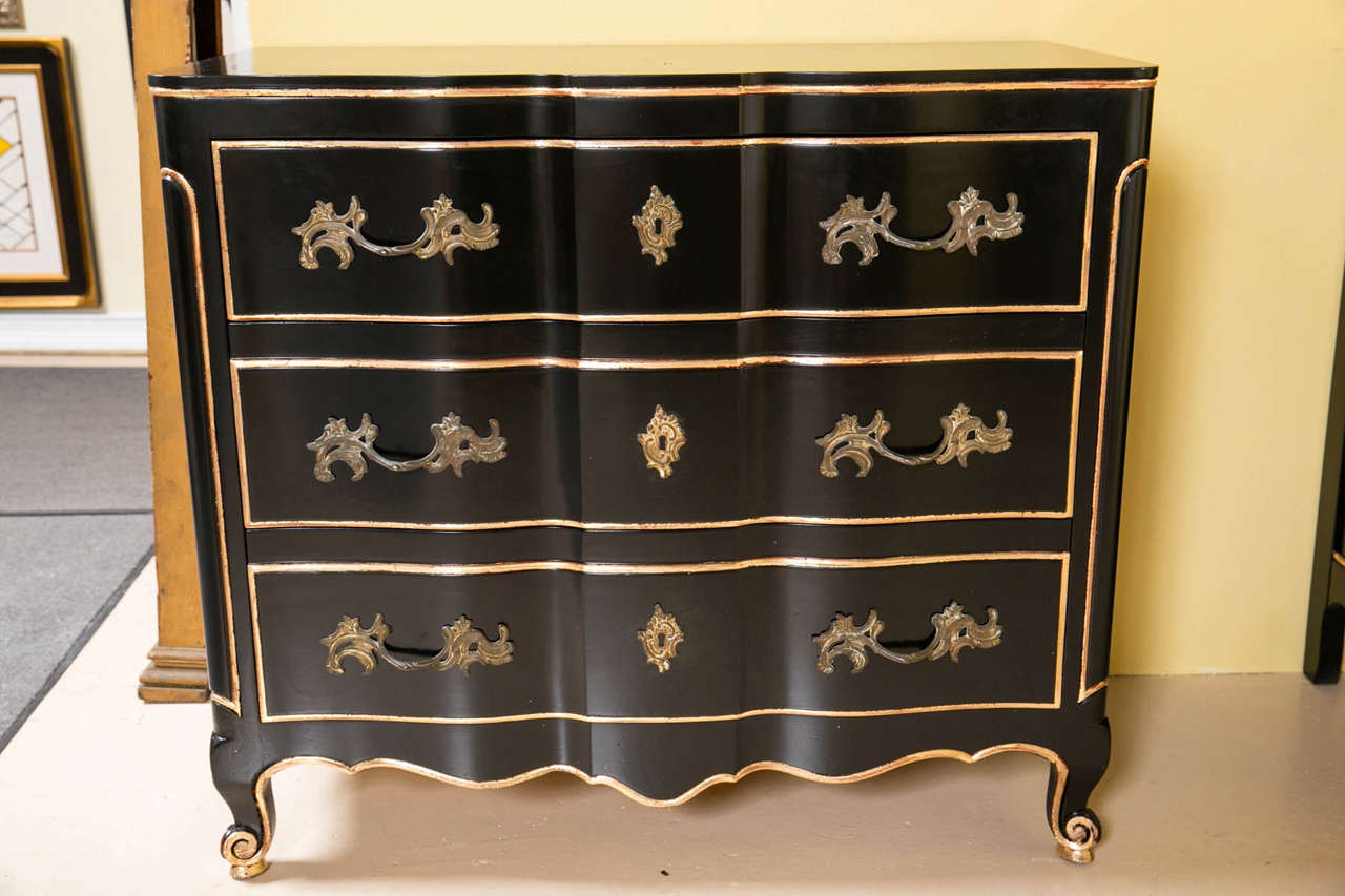 Pair of ebonized and gilt gold Louis XV style commode chests. A fine custom quality pair of ebony chest with gilt gold decorations. The Hollywood Regency serpentine front case having three drawers with bronze pulls. The pair on scrolled apron