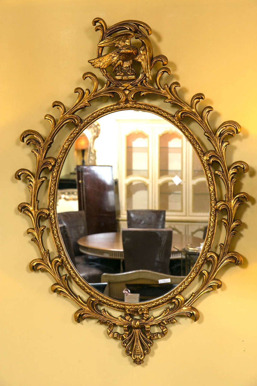 A Georgian style gilt carved mirror adorning a carved eagle. The central oval framed mirror beautifully set in an exquisitely carved frame of vines, leaves and ribbon. The top adorning a wonderfully carved giltwood representation of the winged