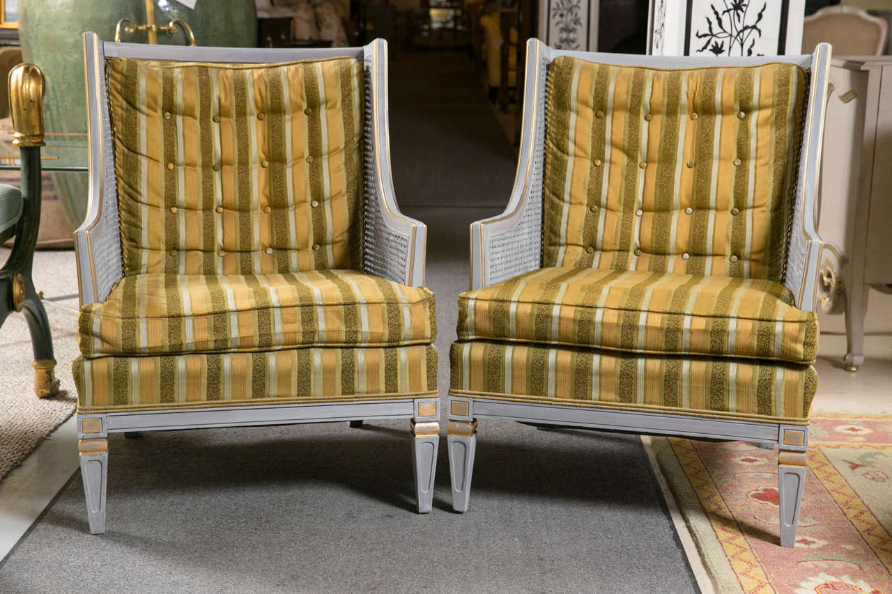 Pair of Statesville, Swedish painted armchairs. The soft distressed gray frames having wonderful gilt gold decorative highlights. Made of solid walnut construction with caned sides and aerodynamically curved arm rests. The upholstery appears to be