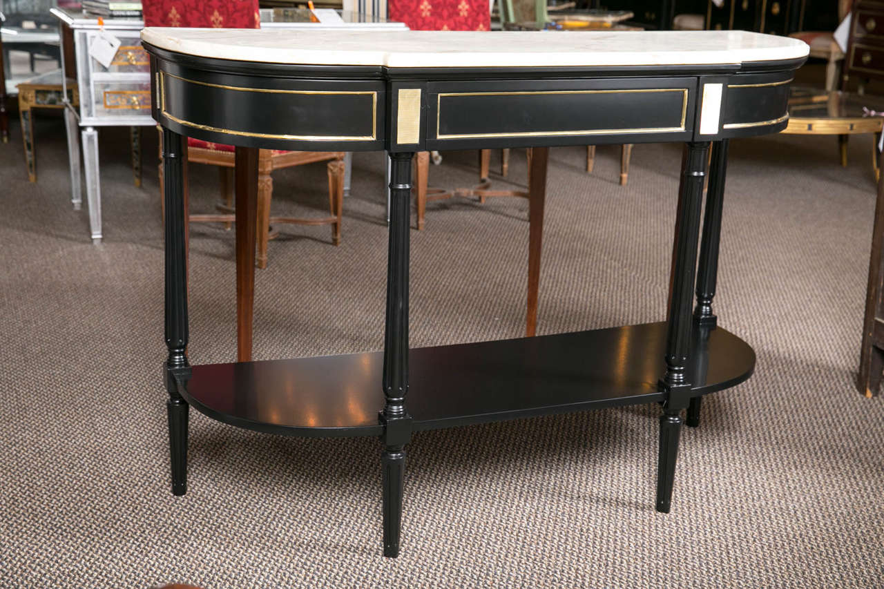 A Louis XVI style ebonized console table by Jansen. This Fine early example of Jansen artistry abounds in simplicity and elegance. The lower shelf area and upper casing supporting a white marble top. The apron having one center drawer flanked by