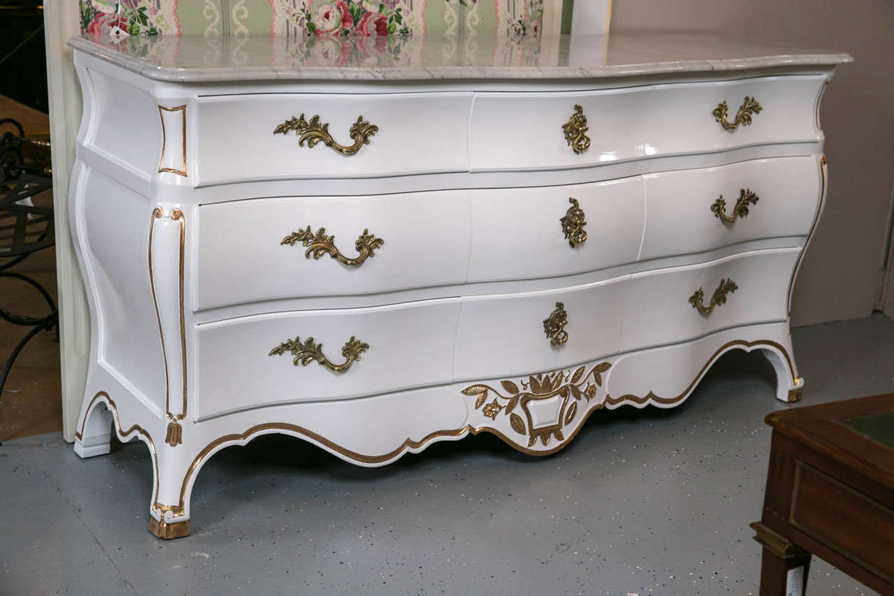 Une commode de style Louis XV à décor blanc et or doré. Le plateau en marbre de Carrare veiné blanc et gris, d'un pouce d'épaisseur, est soutenu par une base de commode laquée blanche. La caisse comporte un groupe de trois petits tiroirs centraux