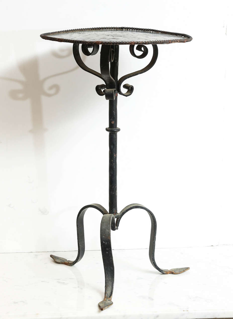 Iron martini table with hammered circular top has a small rope design around the top edge as well as scroll shaped supports and arrow shaped feet.