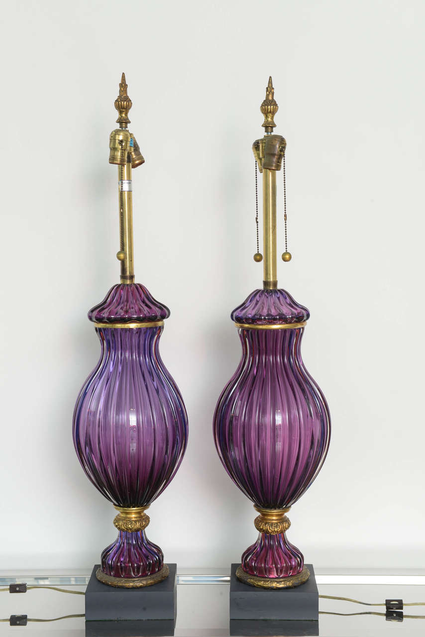 Pair of large purple fluted Murano glass lamps with a black square bases. The lamps have gilt metal hardware. One lamp features the original Marbro label near the lamp sockets. The widest part of the glass measures: 9 inches.