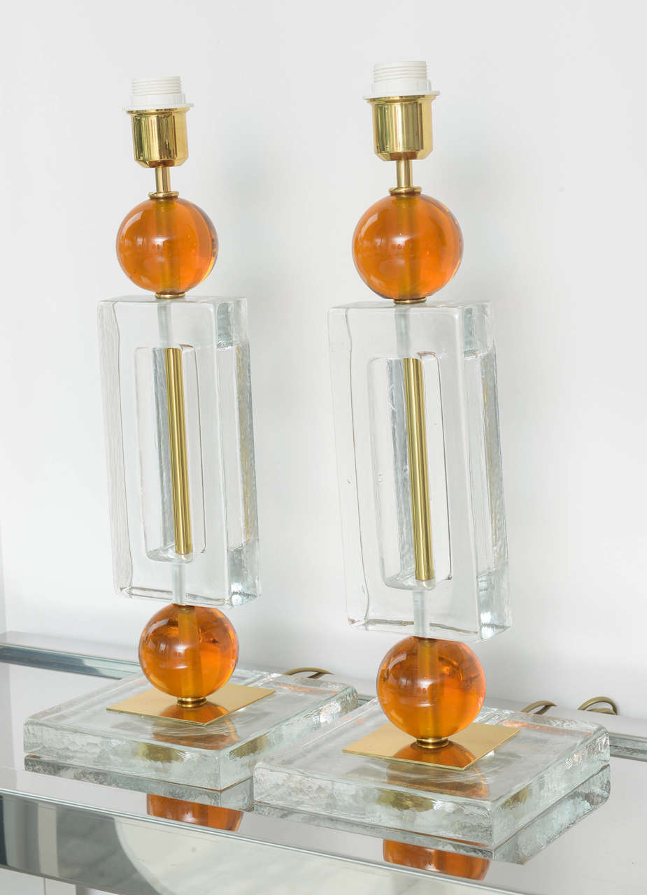 Pair of two-tone clear and orange Murano glass lamps with a brass rod detail running through the, and becoming a feature of, the negative space in the main rectangular component.. The lamps are wired for US standards and functioning.