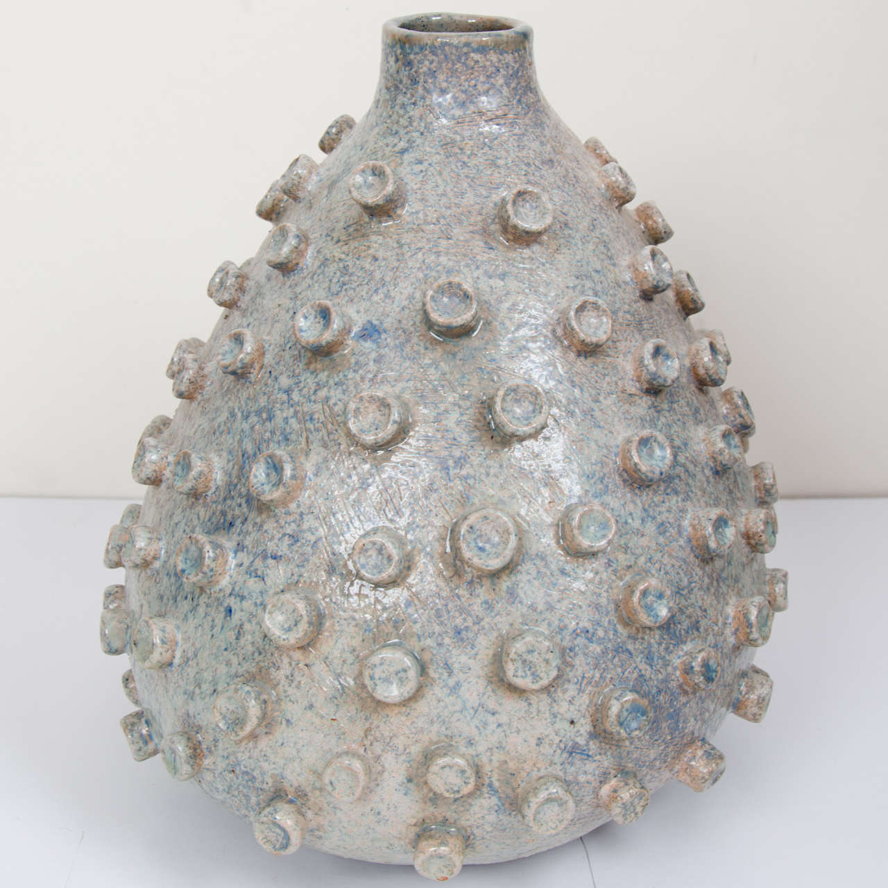 The handmade stoneware vase has a round bulbous shape that is asymmetrical with a narrow funnel opening. The surface of the vessel is covered in round rings emphasizing its organic form.