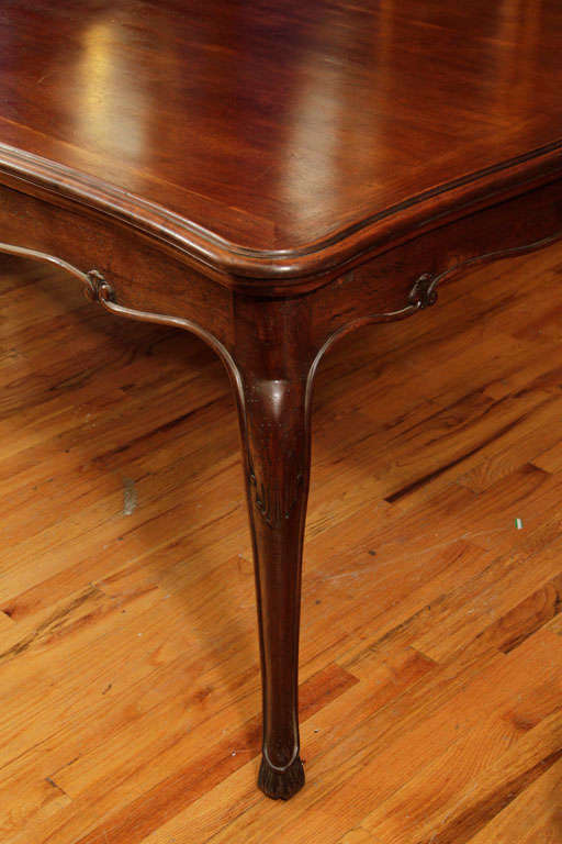 A cherry wood dining table with retractable leaves at each end.The piece has a curved skirt with carved leaf deatails and cabriole legs.