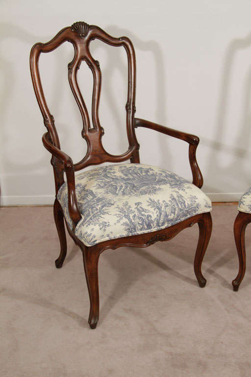 A set of 8 dining chairs; two with arms and six armless sidechairs. Each has hand carved scrolling details and has been recently re-upholstered in white and blue toile de jouy fabric.