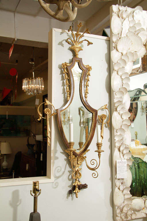 A pair of art deco sconces, each with a mirrored back and two candle form lights. The pieces are elaborately detailed with scrolling vegetal brasswork.