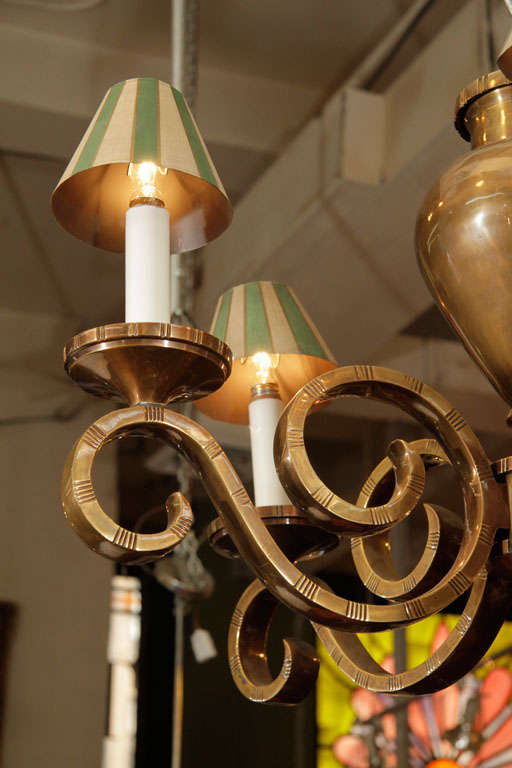 A polished bronze chandelier with five scrolling arms and candelabra form lights. Each light is topped by a striped green and white shade.