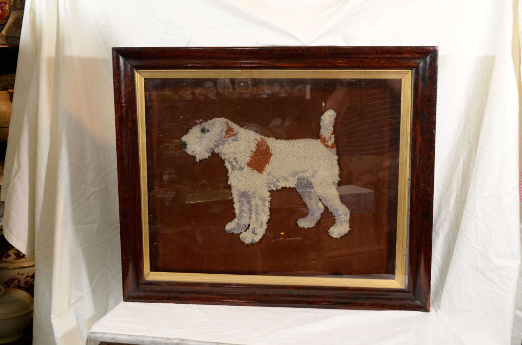 A charming woolwork picture of a wire haired fox terrier set with a glass eye, within an ebonised frame. Woolworks of dogs were very popular in England in the 19th century.