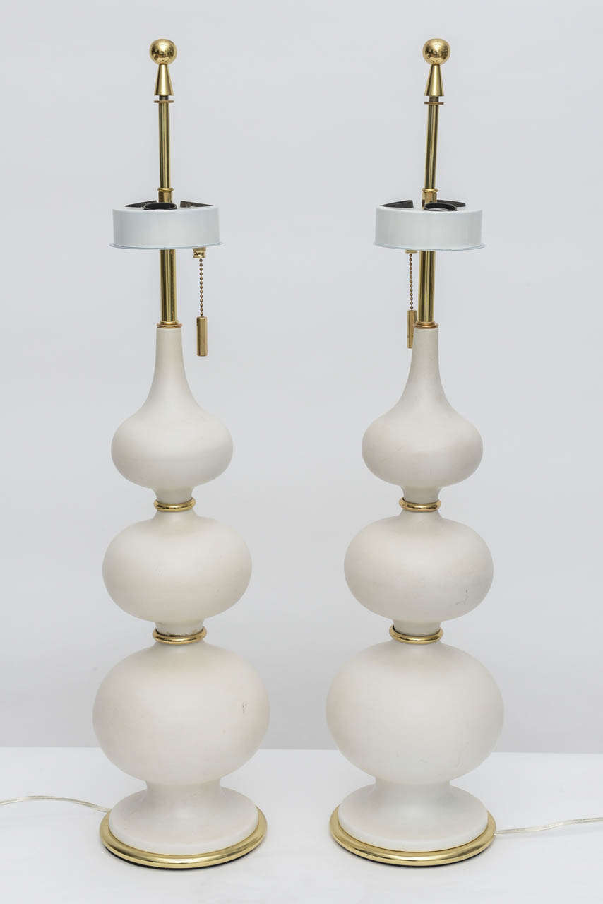 Pair of stacked gourd, matte porcelain table lamps fully appointed with brass fittings. Original brass three-way on/off chain pulls that terminate with brass cylinders. Lamps are complete with original brass finials and triple socket disks.