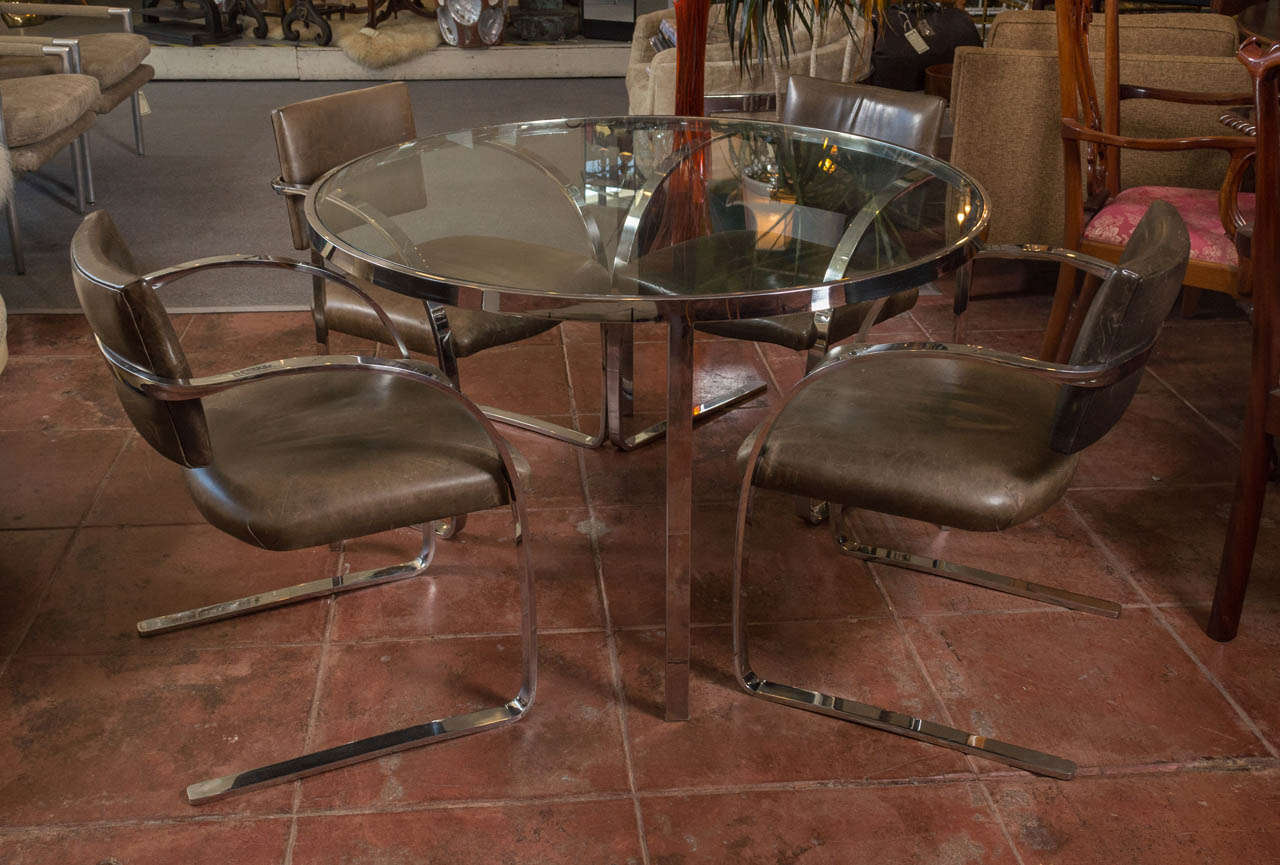 A circa 1988 polished stainless steel and leather dining set by Mark Mascheroni for Brueton, first designed in 1985. The four chairs have fully cantilevered seats, and solid bar stock frames, they have compound bends as the metal twists and sweeps