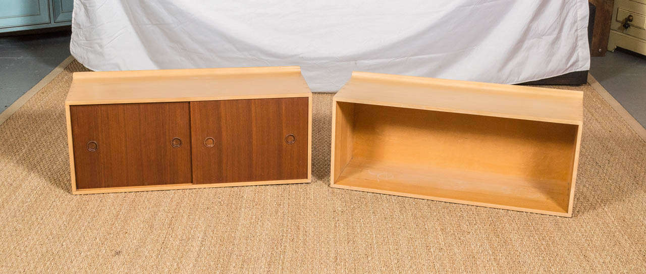 A rare pair of Finn Juhl hanging cabinets for Baker, these were only produced for a few years at the start of the 1950s. One has two sliding doors of Teak, with the other an open cabinet. Both have the oval Baker metal label on their backs. 
Both