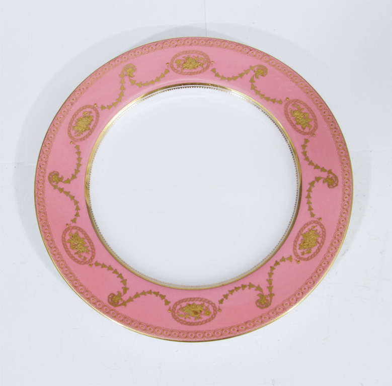 A set of twelve dinner plates by Spode. Each has a pink outer ring with gold floral details. Stamped spode on the bottom.
