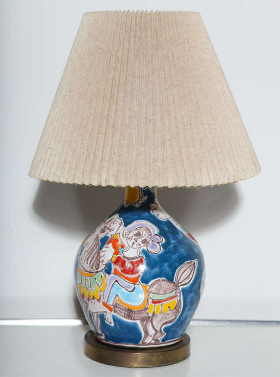 DeSimone hand painted Blue, Red and Purple Glazed Art Pottery Table Lamp. Featuring a wide, reflective bottle form on round patinated Brass base with hand rendered lighthearted scene with hands free girl on horse with flower.  WIth bright Blue