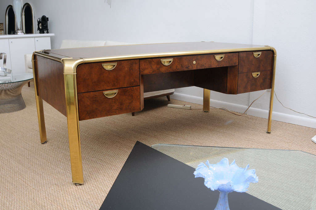 Exquisite burl wood and high polished brass executive desk with inset drawer pulls. Five drawers in total; one large drawer for files. Original lock and key in working order. The feet have adjustable levelers. Desk is finished on all sides so it can