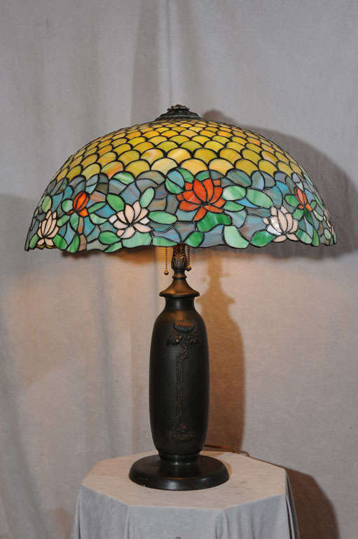 This impressive, large leaded glass lamp was executed by the Chicago Mosaic Company.  It offers beautiful upper portion of scalloped greenish-yellow tiles and the irregular border consisting of flowers of red, orange, and white.  The background