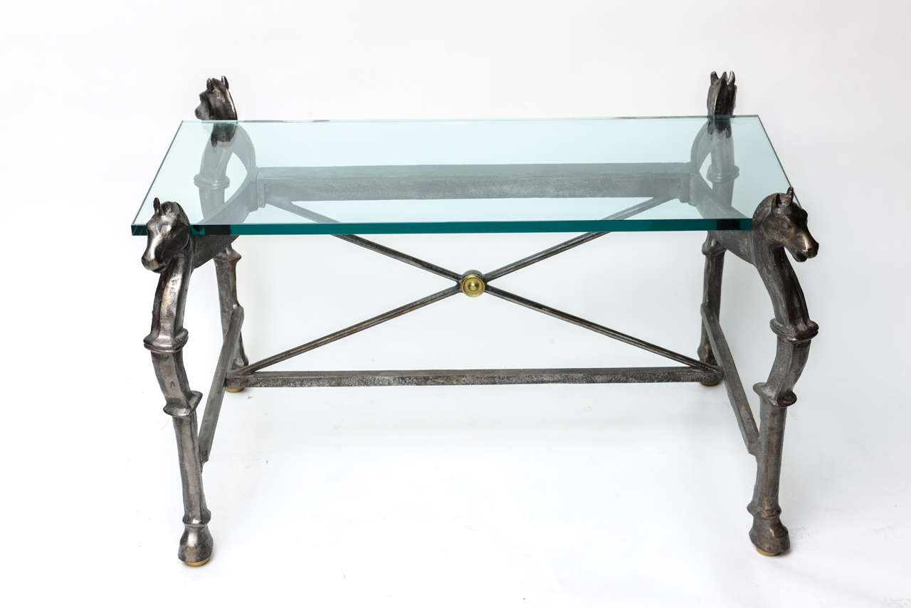 Heavy steel and brass cocktail table with horse heads supporting the thick glass top and hoofed footed legs.