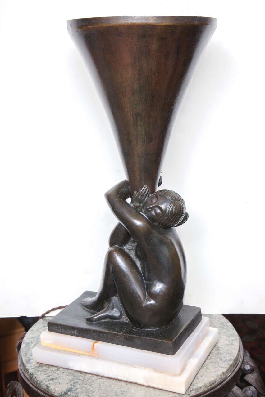 Georges Henri Tribout (1884-1962). 
French Art Deco table Lamp in patinated bronze, depicting a seated nude woman holding the reflector cone, mounted on a two-tiered onyx base, Signed 
