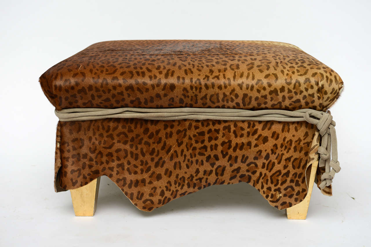 The Ronn and Mars Jaffe design ottoman or cocktail table from the 1970s, is covered in exotic leopard patterned stenciled calf hair overlay in pelt style, suede multi-welt wrapped centre with hanging knotted ties on one corner, and gilt