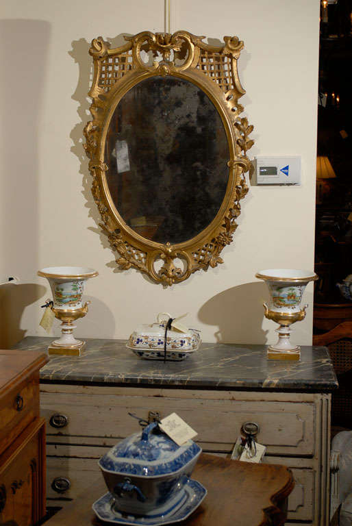 A gilt-wood oval mirror with carved flowers, fretwork design and aged mirror.



