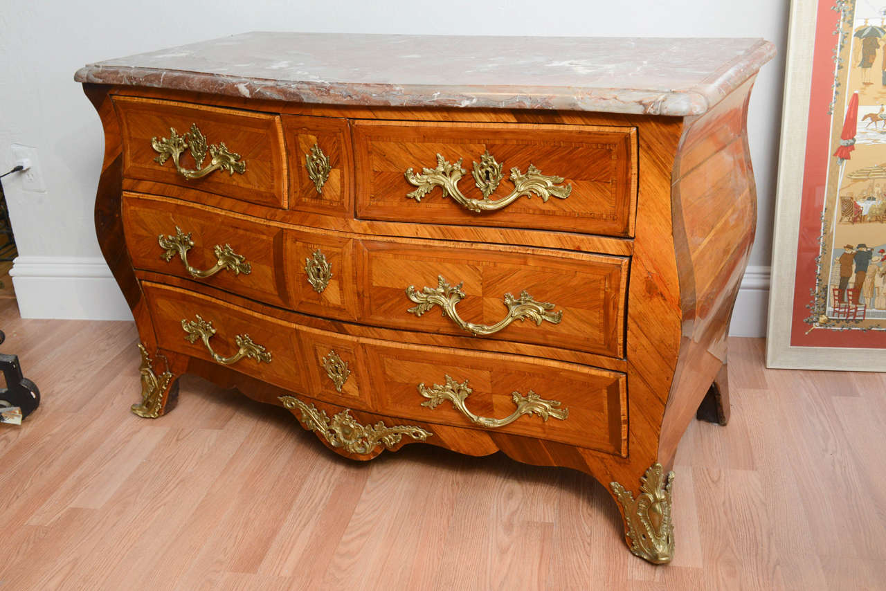 Lovely four-drawer 18th century commode with beautiful marquetry. Striking bronze mounts and pulls. Rose/grey veined marble top.