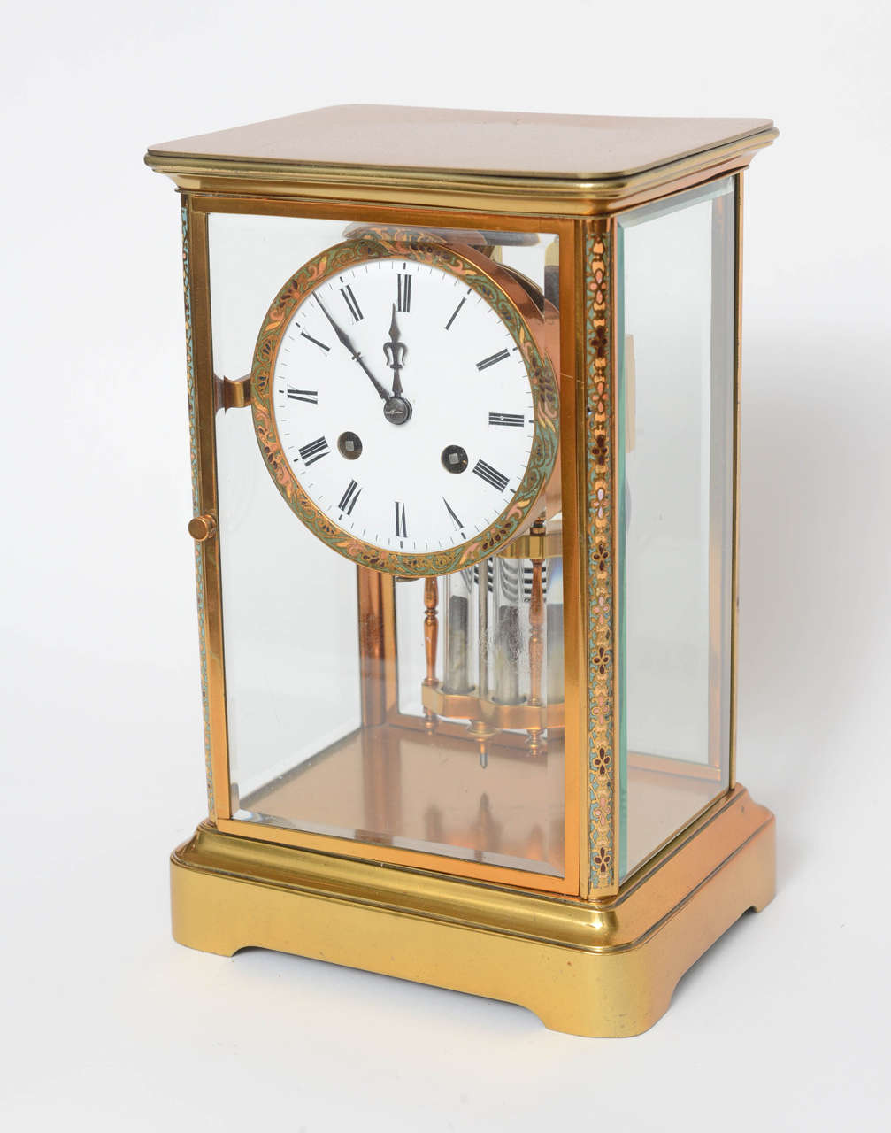 Regulator mantle clock, executed in gilt bronze and glass, having a regulator top with champlevé running frieze on either side of the beveled glass case & the white enamel dial with Arabic numerals, the whole rising on a plinth base, retains the