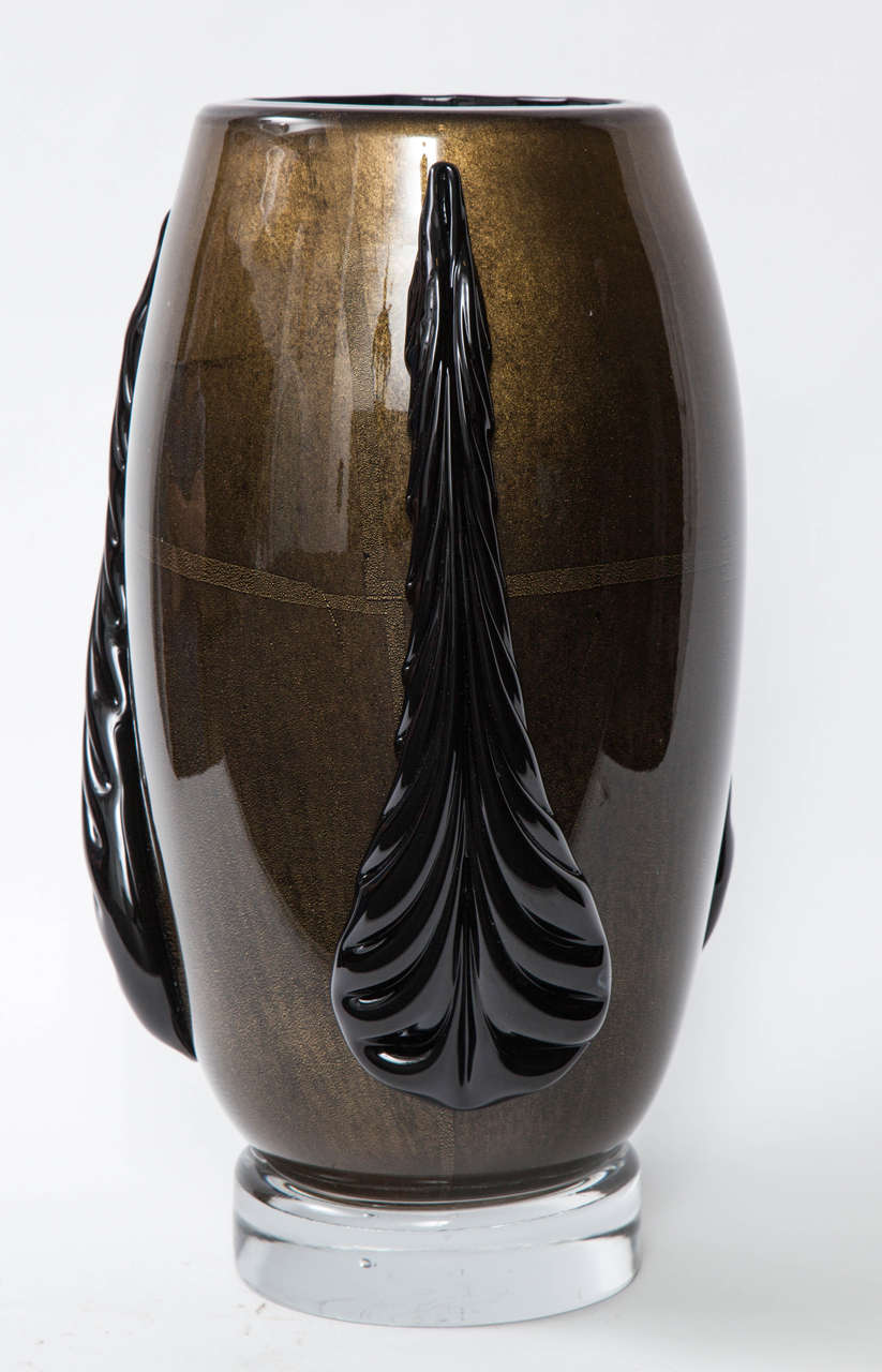 Art Deco inspired vase made of black Murano glass with 22-karat gold dust outer layer and applied black glass stylized leaf forms, sitting on thick clear glass bases. Exquisite craftsmanship. Signed on bottom. 

Currently a pair is available.