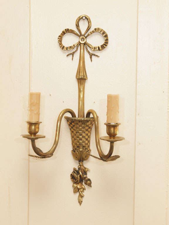 Lovely and delicate pair of two-armed French bronze sconces with basket-weave urn motif from which the arms project. Flowers and leaves protrude from the urn base. The arms are decorated with leaves and terminate in beeswax sleeves. The urn is
