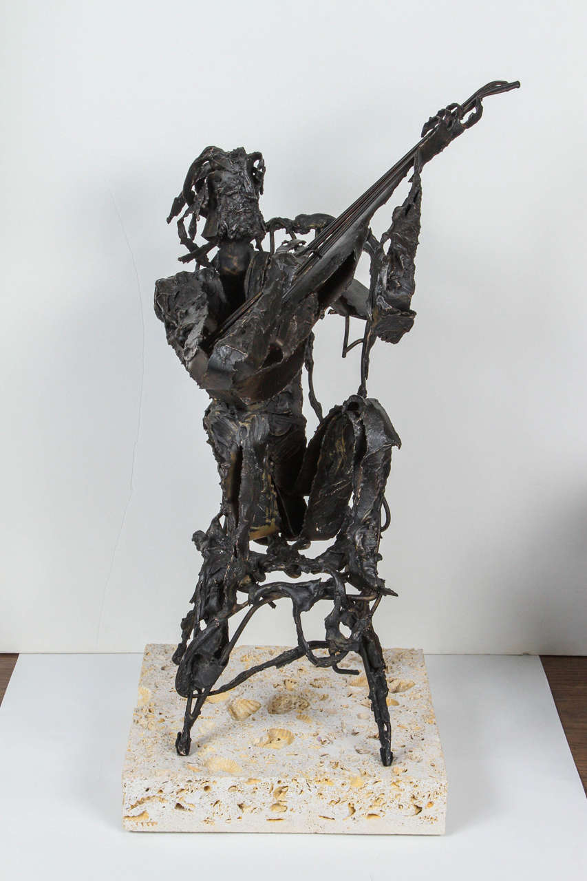 Metal sculpture of man sitting while playing a guitar. Signed: Laster '67. Sits on a shell stone base that measures 10