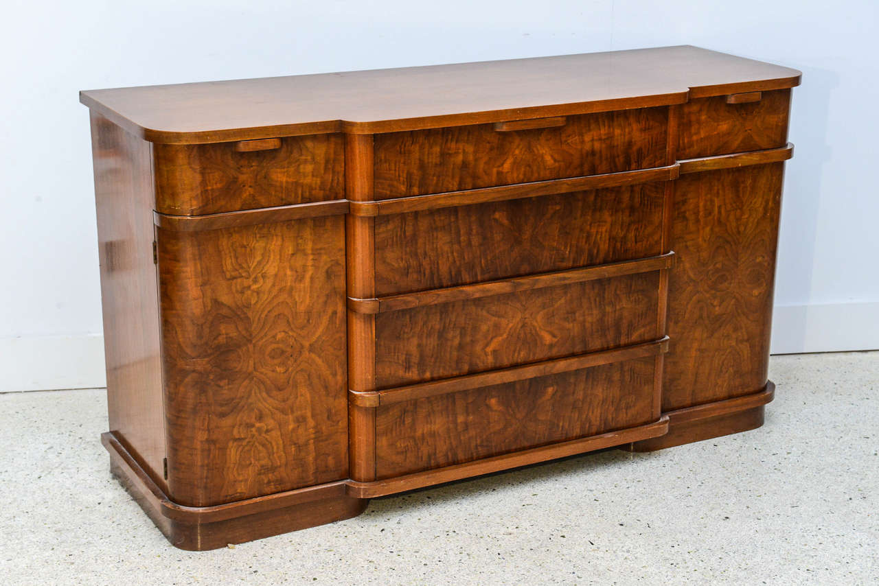 The shaped top above a central bank of four drawers flanked by two cabinet doors on a plinth base, all veneered in a fine flame mahogany.