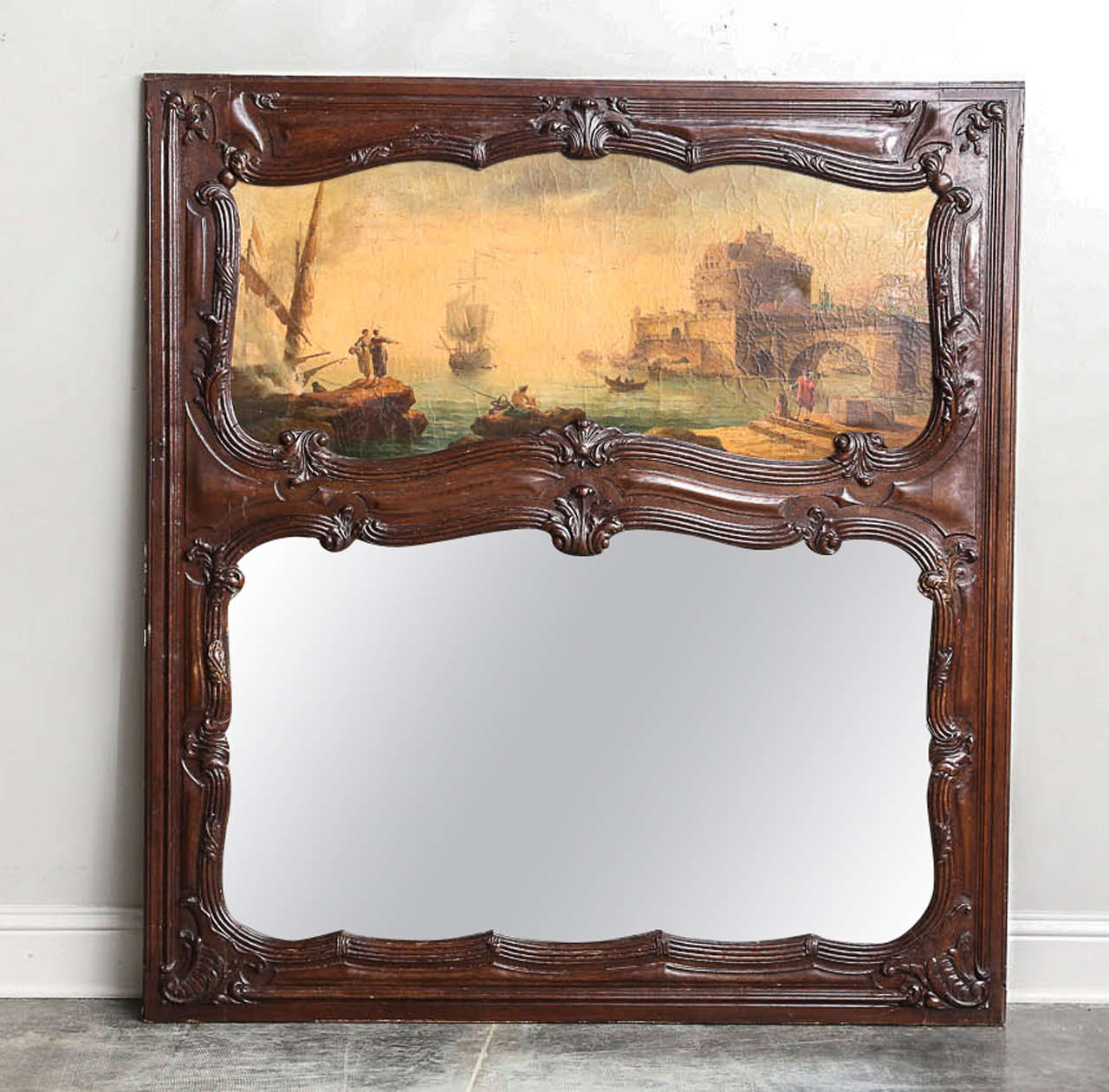 Remarkable 19th century overmantel trumeau with carved wood frame and old mirror. Original oil panting depicting 18th century port scene. Exceptional carved detailing on the frame makes for a truly one-of-a-kind piece of art. 

Established in