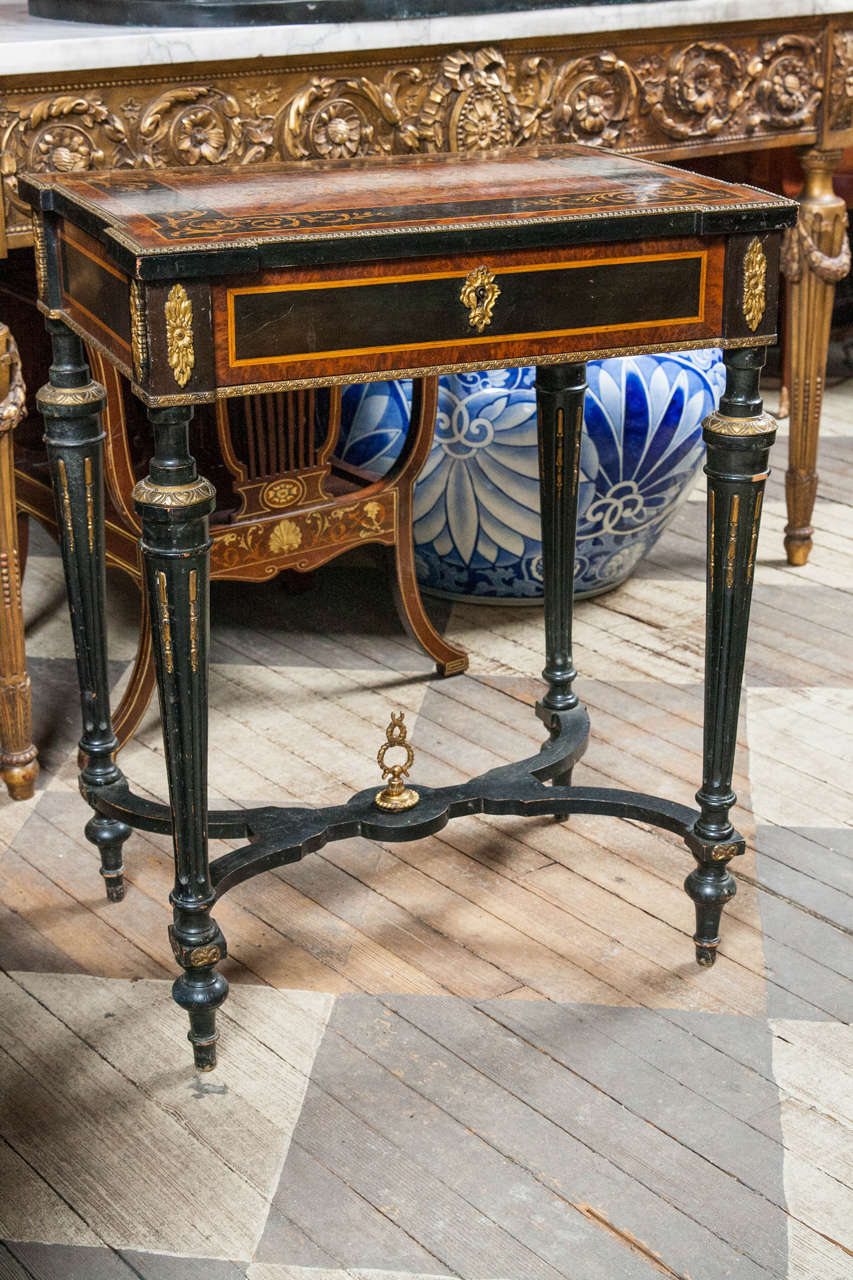 Dating from the Victorian era, this Louis XVI lift top vanity is made of rosewood, satinwood and ebony. The lift top marquetry decorated with swirls and arabesques, and a central urn on a corbel. Inside is a bevel edged mirror framed in gilt bronze.