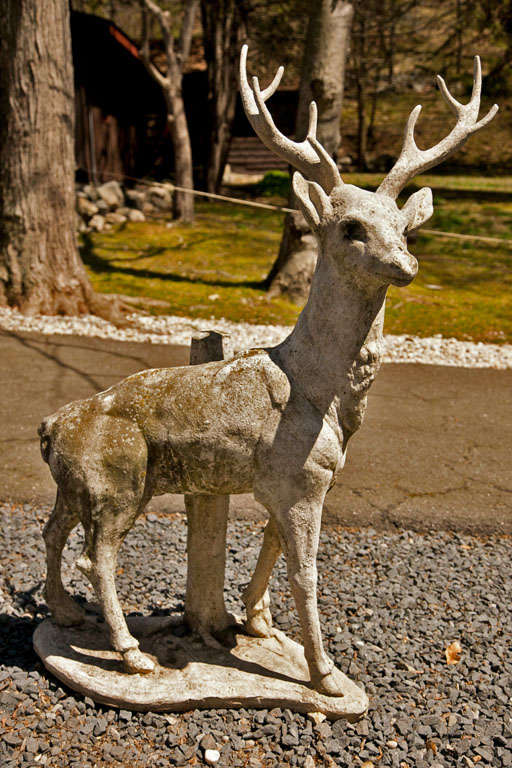 Cement garden statue of a stag standing in front of a base of a tree