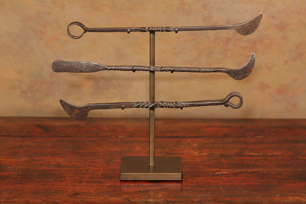 A set of three Chinese forged iron tools. Probably made for use by a leather worker or cobbler, the implements ornamented with twisted handles. Mounted on a single custom bronze stand which allows each tool to be rotated.